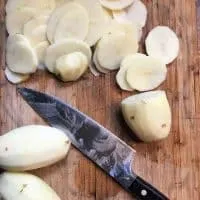 thinly sliced potatoes and knife on cutting board