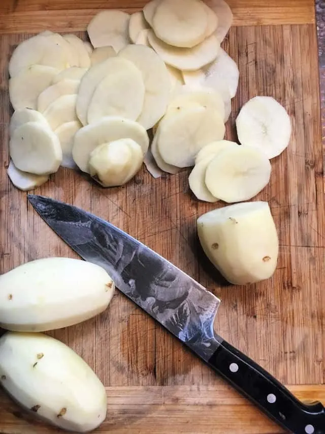thinly sliced potatoes and knife on cutting board