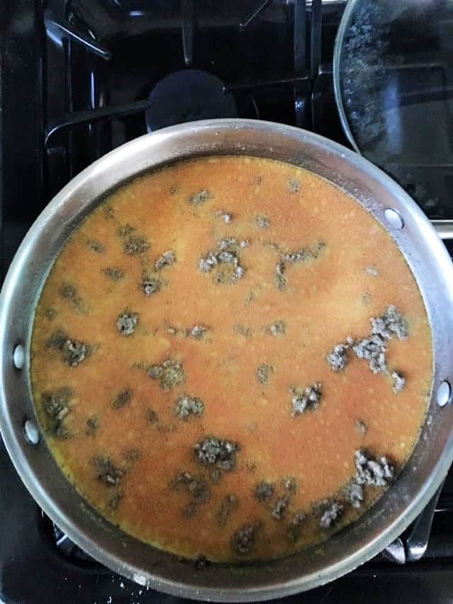 hamburger in pan with sauce on stovetop.