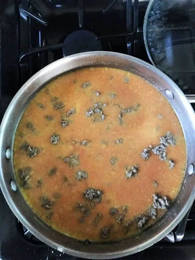 hamburger in pan with sauce on stovetop.