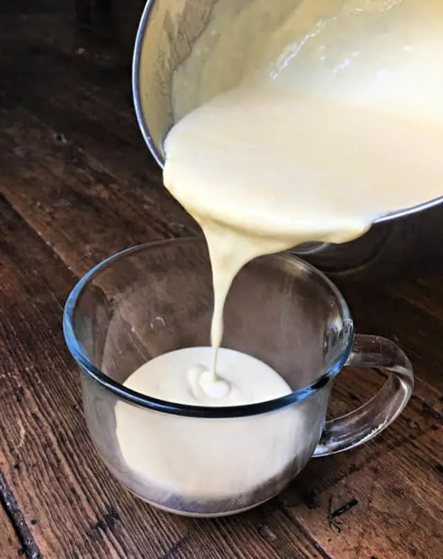 pan pouring cheese sauce into a cup