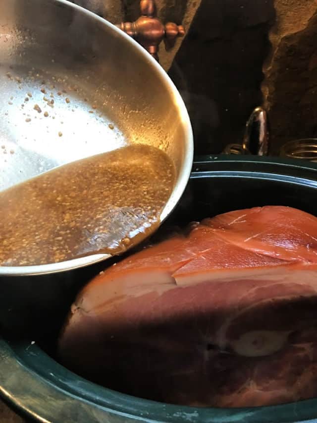 pouring the sauce over the ham in the crockpot