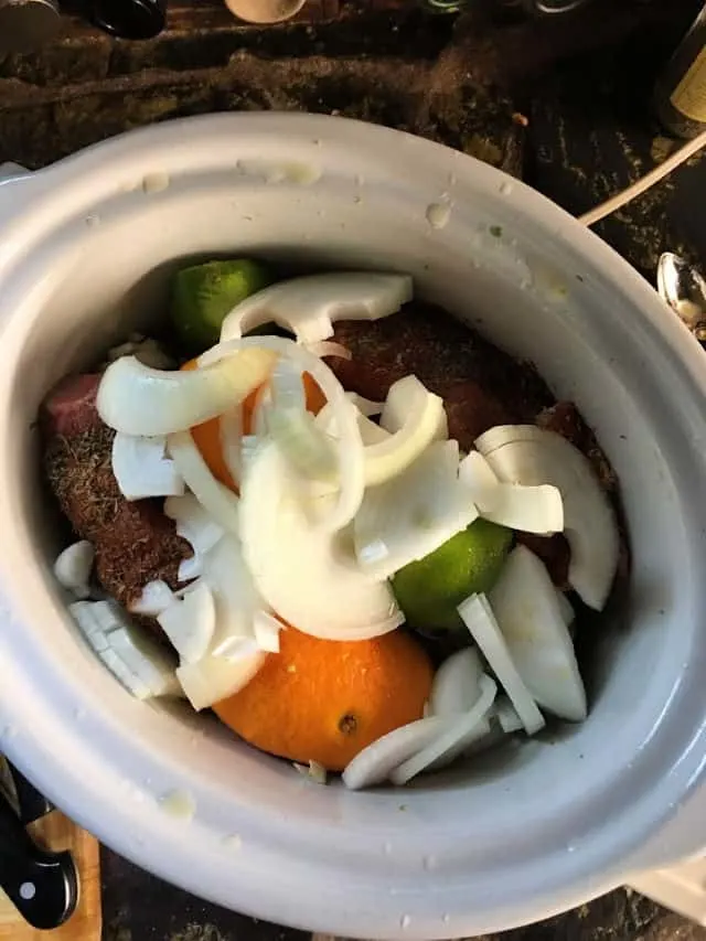 crockpot full of cuban pork ingredients, onions on top