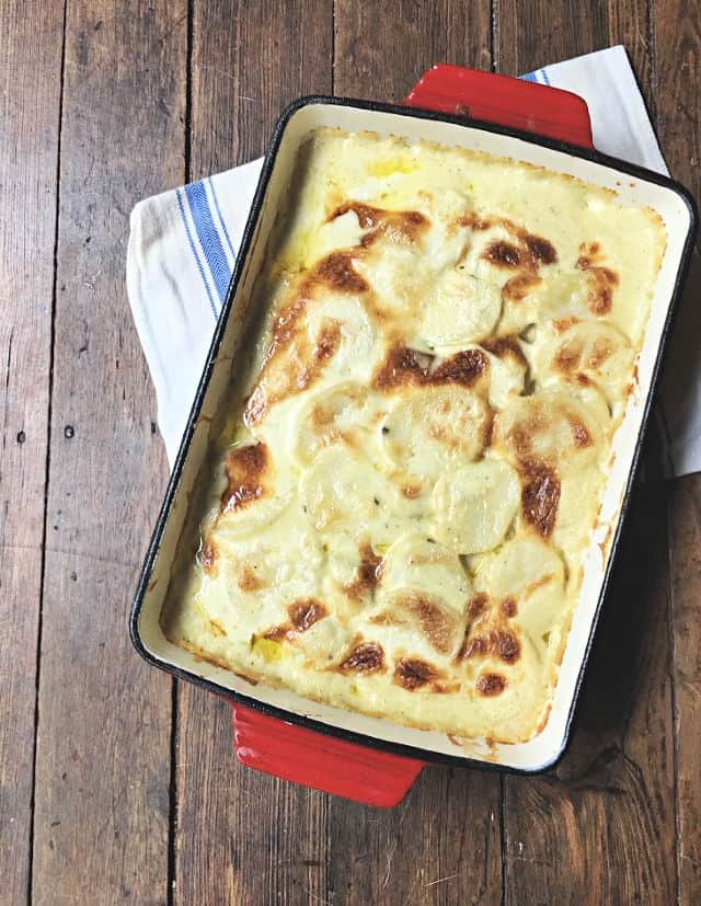 red pan of creamy scalloped potatoes on white towel