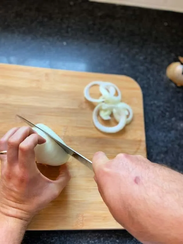hand holding onion and the other cutting it into rings