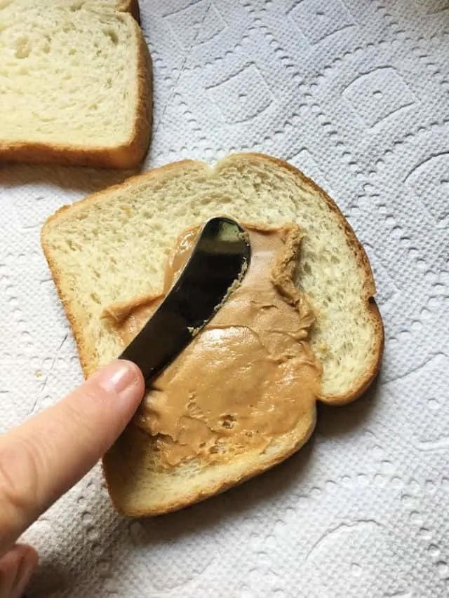 knife spreading peanut butter on bread