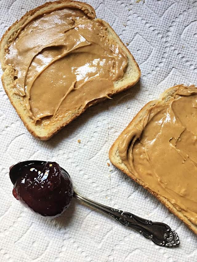 peanut butter on two slices of bread with teaspoon of jelly