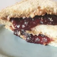 Jam falling out of sandwich onto blue plate