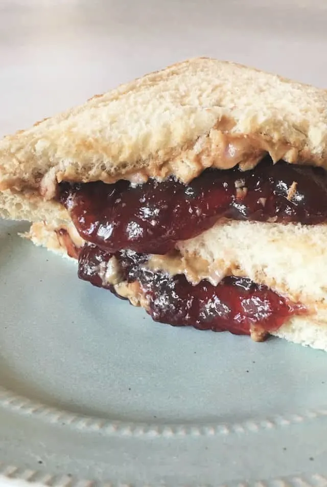 Jam falling out of sandwich onto blue plate