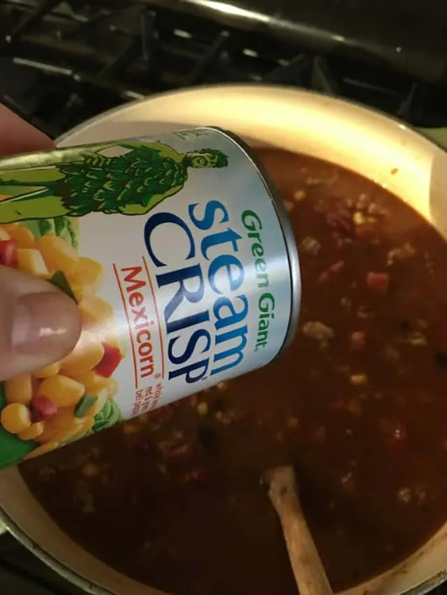 can of mexi corn being added to stockpot of soup