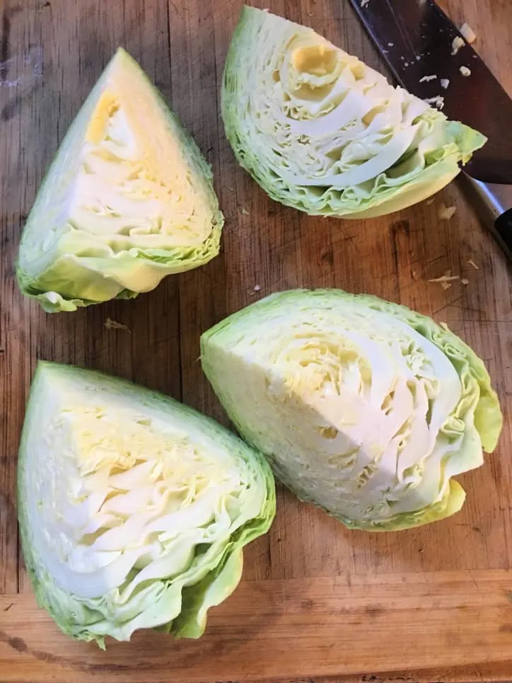 head of cabbage cut into fourths with knife on cutting board