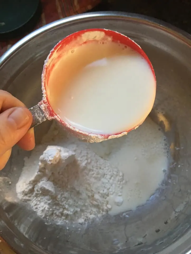 measuring cup of milk over a metal bowl of batter ingredients
