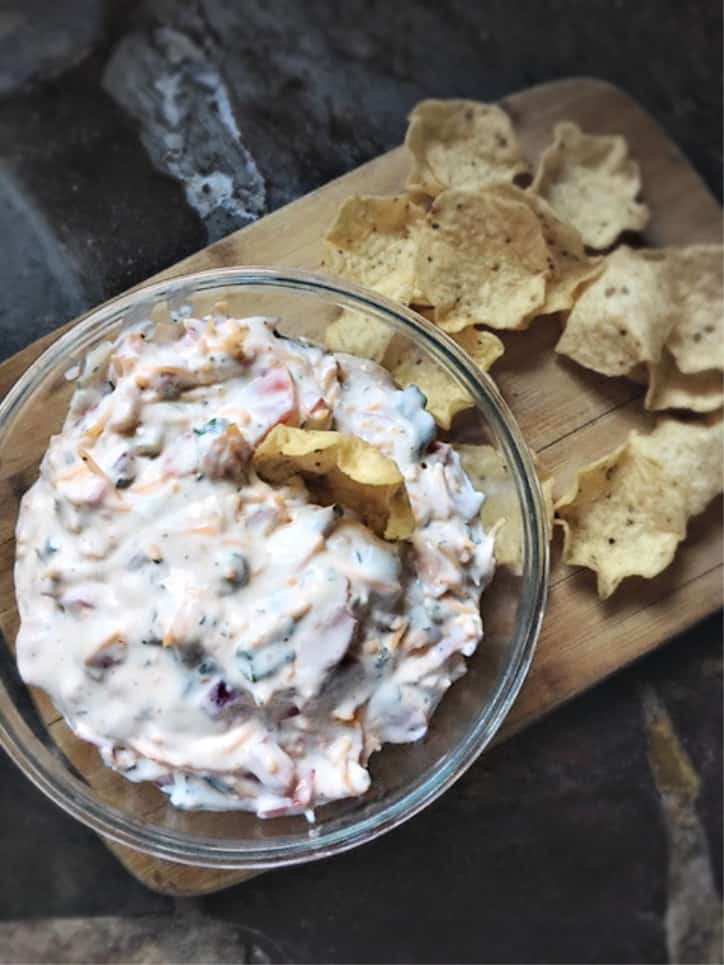 glass bowl of dip with tortilla chips and cutting board