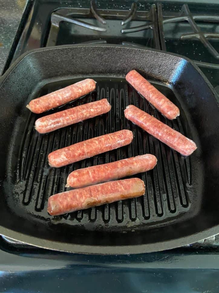 raw sausage links on a cast iron grill pan.