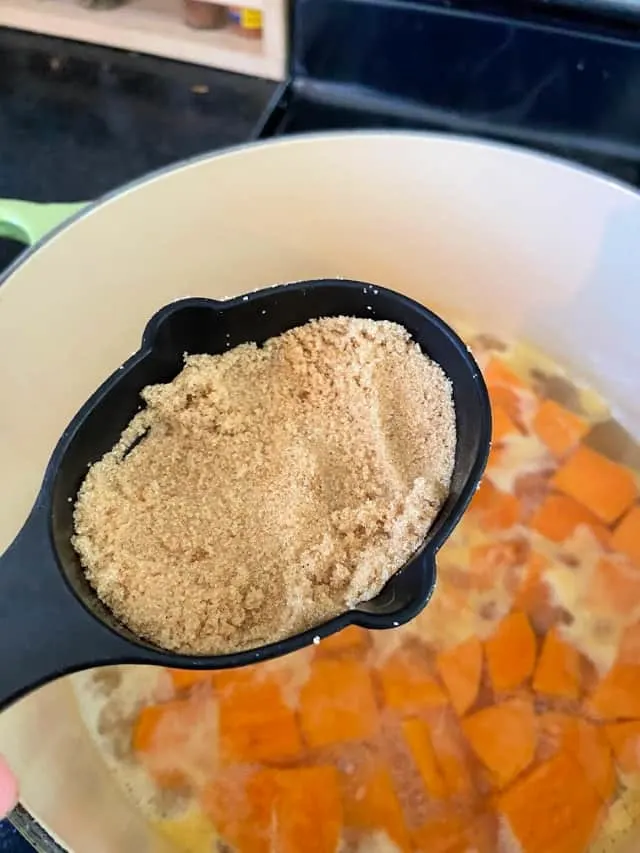 measuring spoon of brown sugar over pot of sweet potatoes