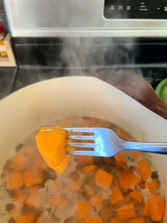 fork piercing sweet potato over large pot of cooked sweet potatoes