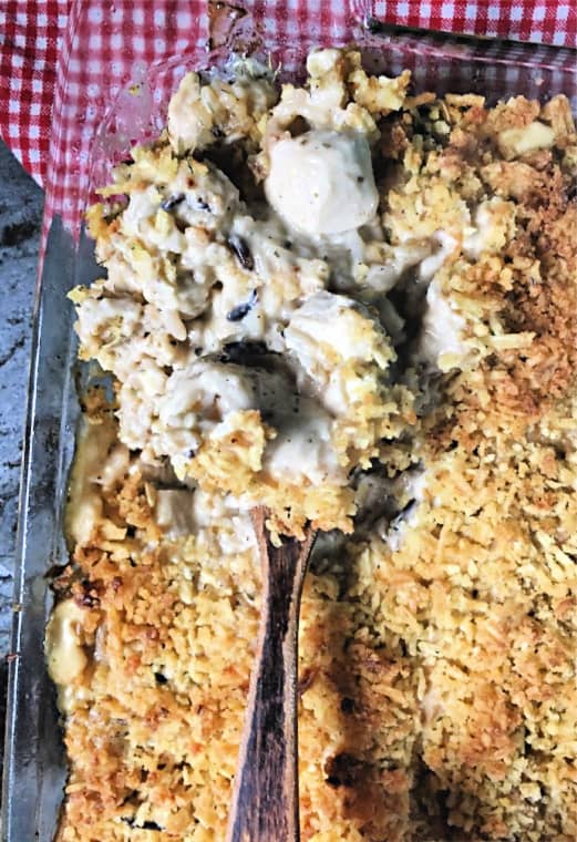 wooden spoon dipping casserole with checkered napkin in background