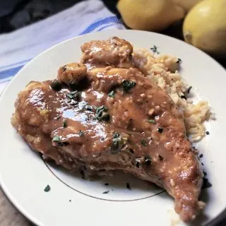 piece lemon chicken piccata on plate with rice and lemons to side