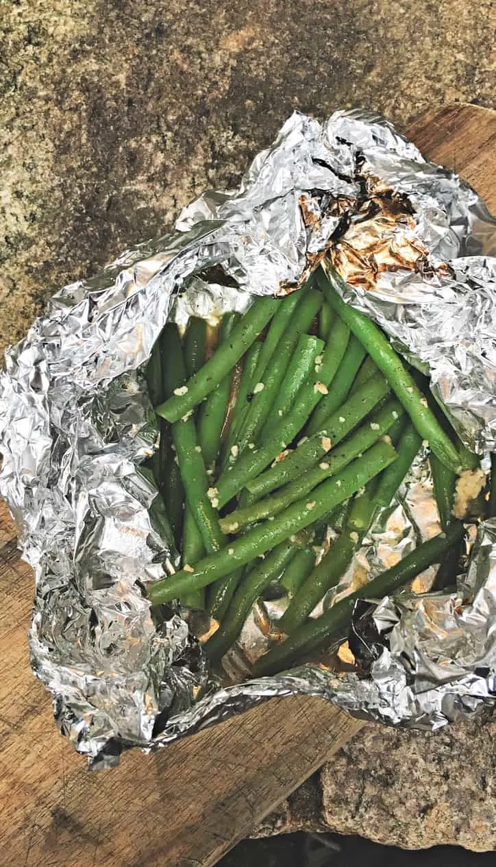 overhead shot of green beans in foil packet with scorch marks on foil