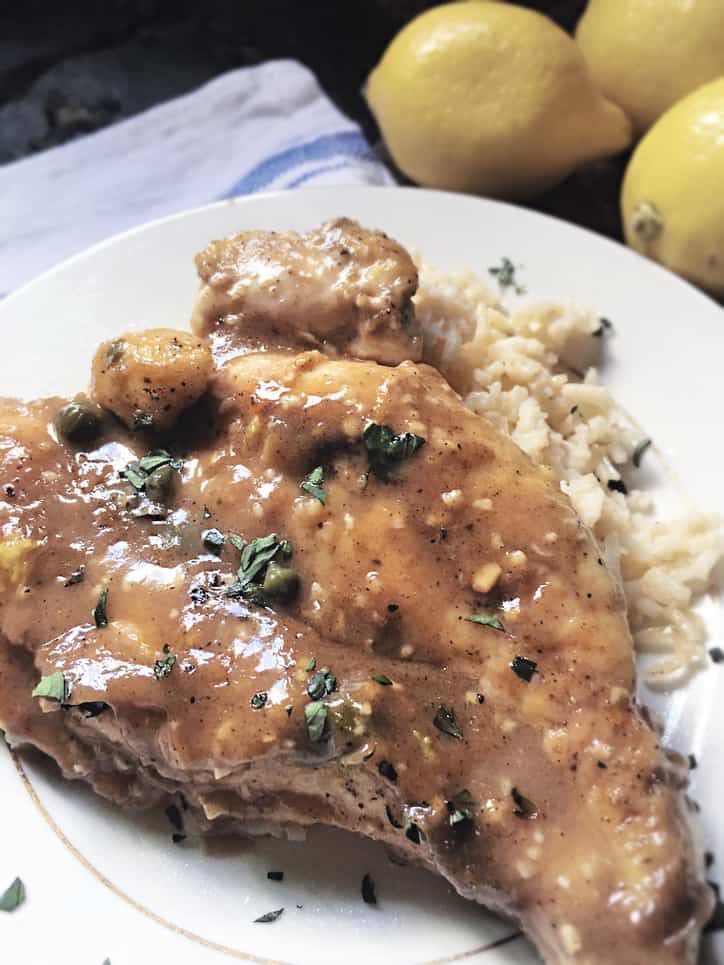 close up of lemon chicken piccata on small white plate with rice