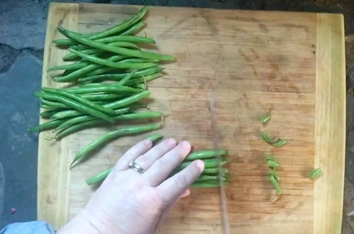 hand cutting the ends off of green beans on cutting board