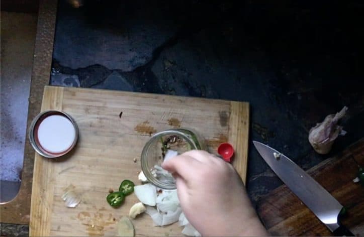 hand adding spices to ball jar