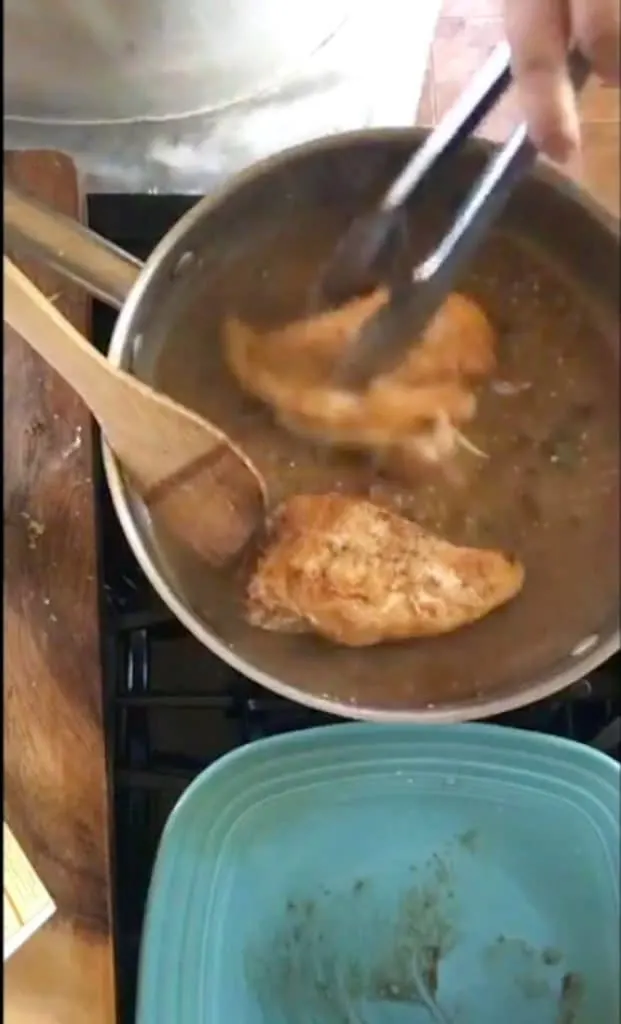 tongs adding chicken breast to sauce in pan