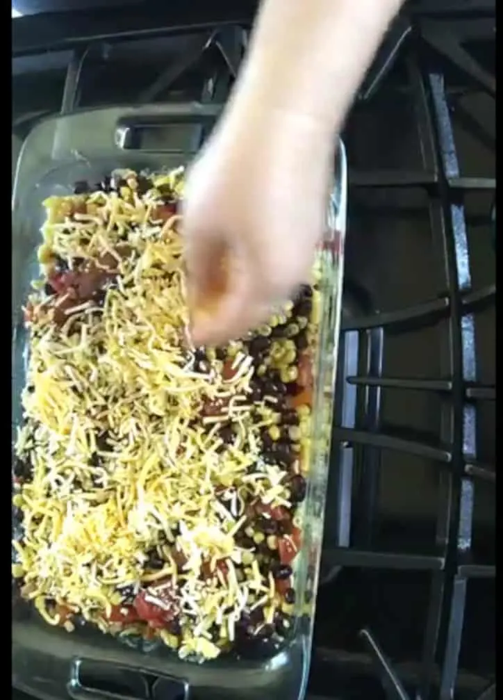 hand spreading shredded cheddar cheese over the top of easy taco bake casserole