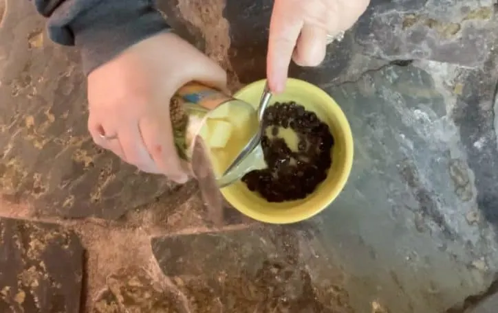 yellow bowl of raisins with hand draining pineapple juice into bowl