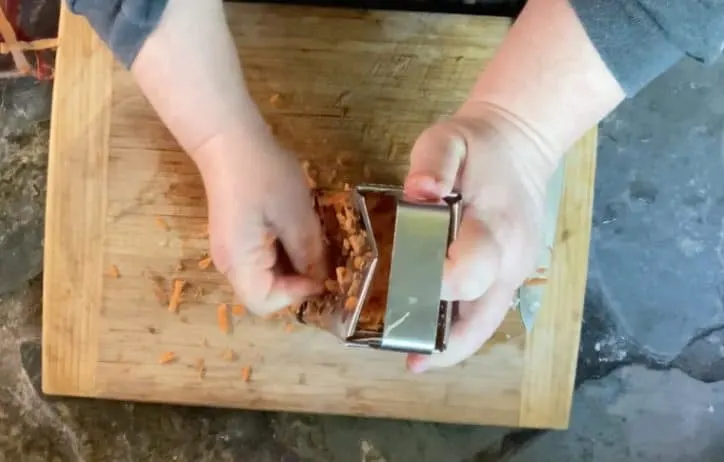 2 hands grating carrots on cutting board