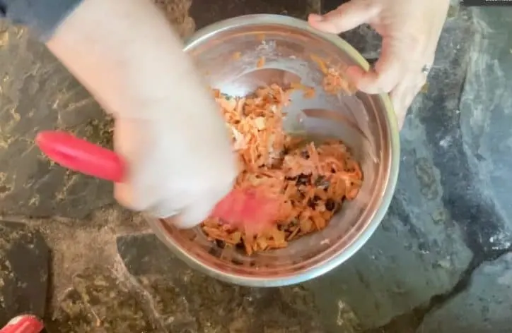 hand mixing carrot salad together with red spatula