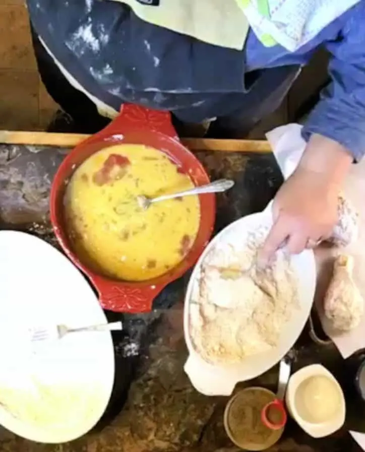 hand using fork to dredge chicken in flour
