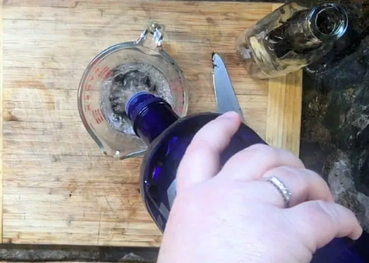 hand pouring blue bottle of vodka into a liquid measure