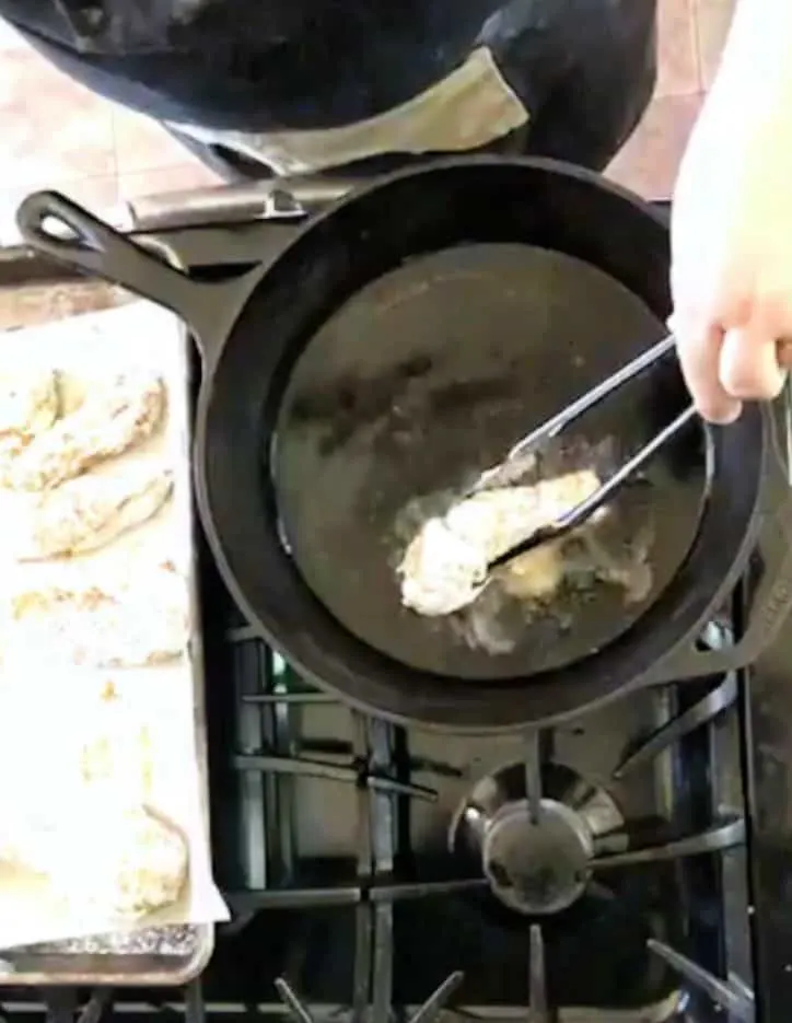tongs adding chicken to hot oil in pan
