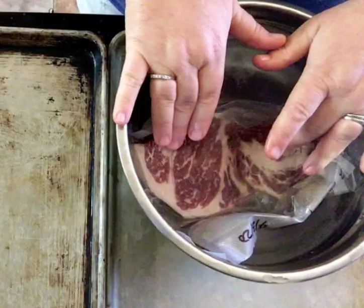 two hands submerging frozen steak into water in a bowl