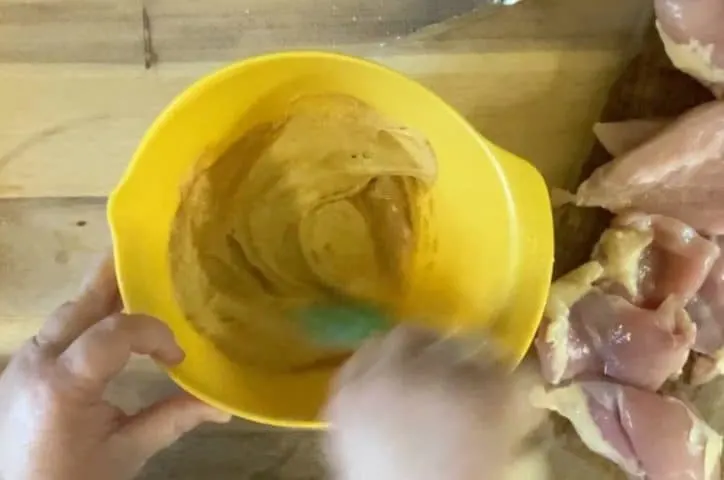 a yellow bowl with two hands mixing up sauce ingredients. 