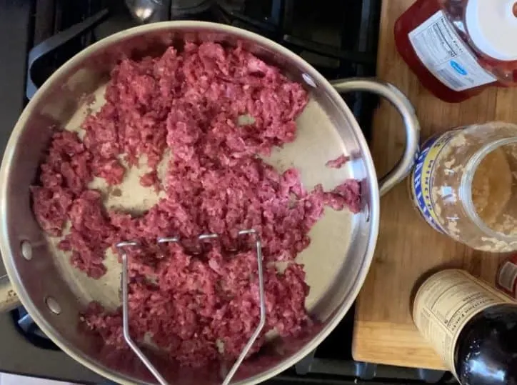 ground beef in a frying pan with a potato masher