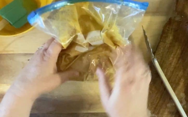 two hands mixing up honey mustard curry sauce and pieces of chicken in a plastic bag