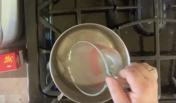 hand adding stock to sauce pan