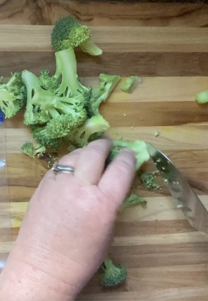 broccoli, hand and knife on cutting board