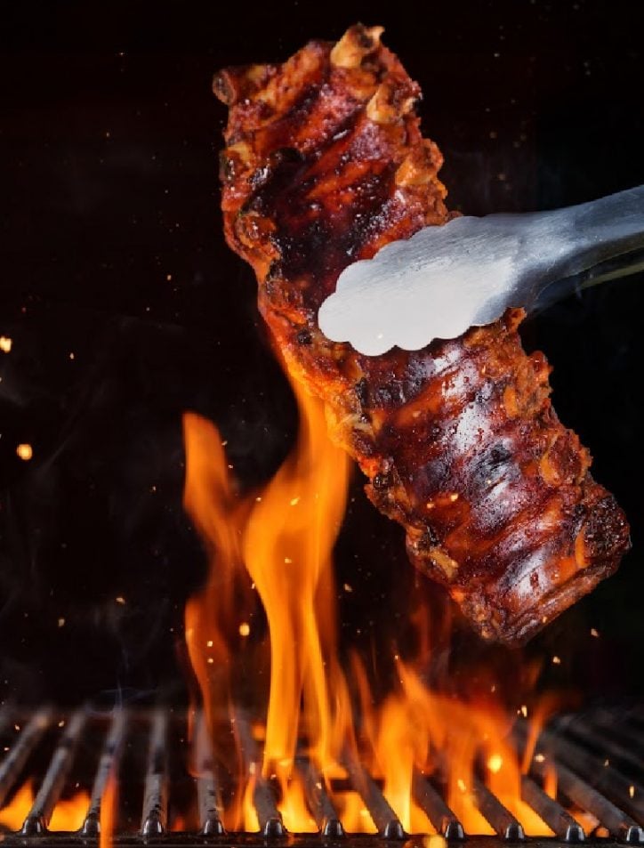 baby back ribs with tongs over fire