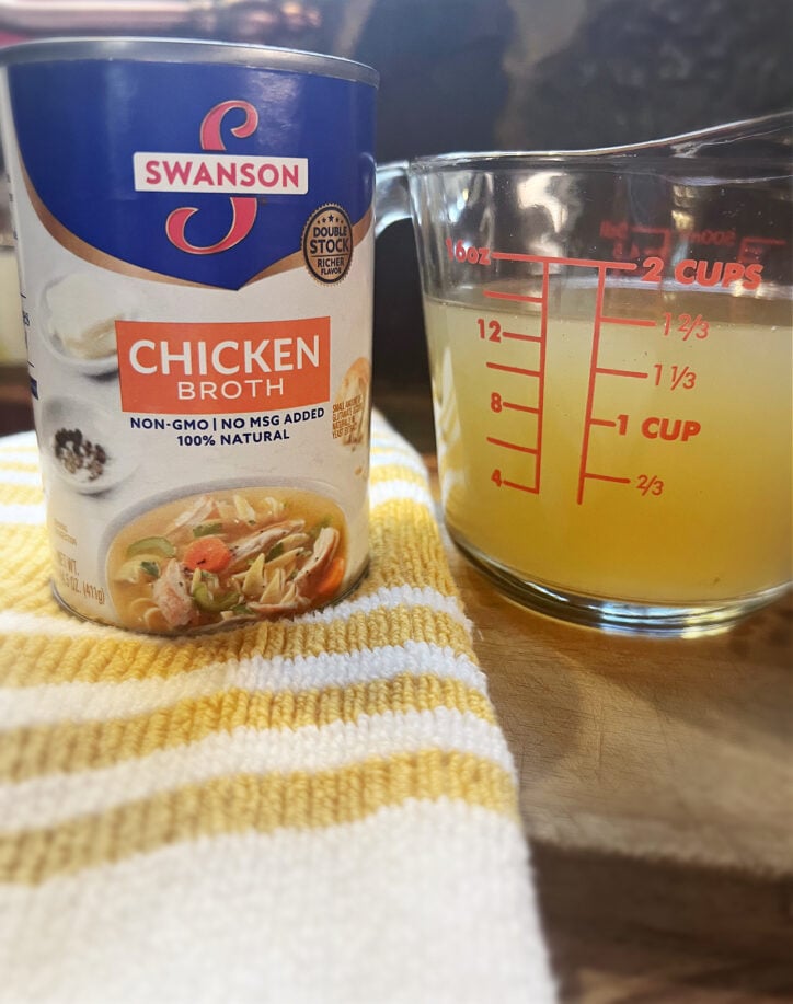 Can of chicken broth and a liquid measuring cup of chicken broth.
