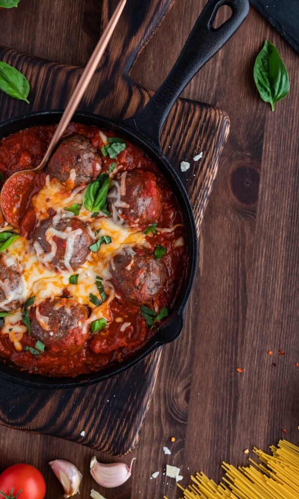 Pan of cheesy meatball bake on cutting board. 