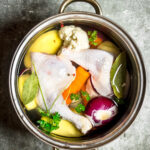 raw chicken, herbs, and vegetables in a pot with water