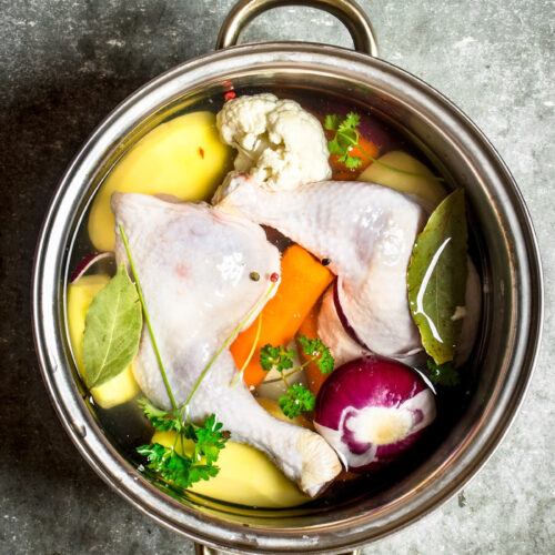 raw chicken, herbs, and vegetables in a pot with water