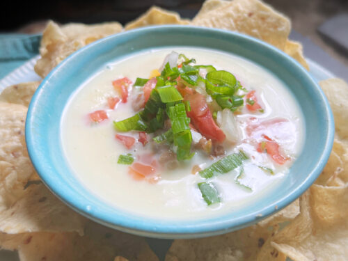 white cheese dip in a blue bowl with tomatoes and green onions on top