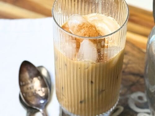 Glass of Vietnamese iced coffee with ice cubes and a sprinkle of cinnamon on top, served in a ribbed glass with a spoon beside it.