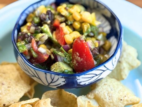 cowboy caviar in a blue and white bowl with tortilla chips on a blue plate