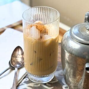 Vietnamese iced coffee in a tall ribbed glass with ice cubes, served next to a metal coffee pot on a wooden surface.