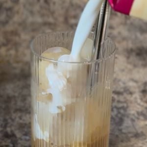 pouring half and half into a ribbed glass with espresso in the bottom